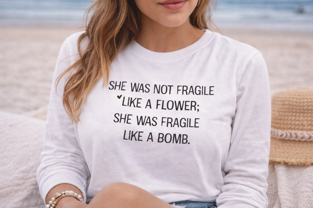 A woman wearing a white t-shirt with text printed on it, sitting on a beach.