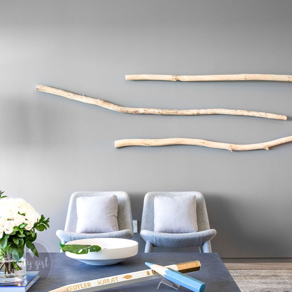 a modern living room with a gray wall, two gray chairs, a white bowl, a vase with white flowers, and a wooden branch wall decoration.