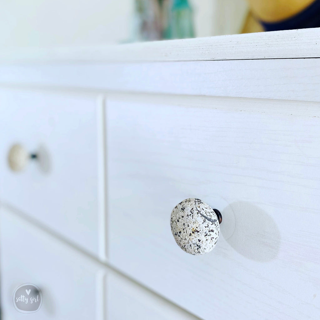 A close-up view of a white wooden drawer with a speckled knob on the front.