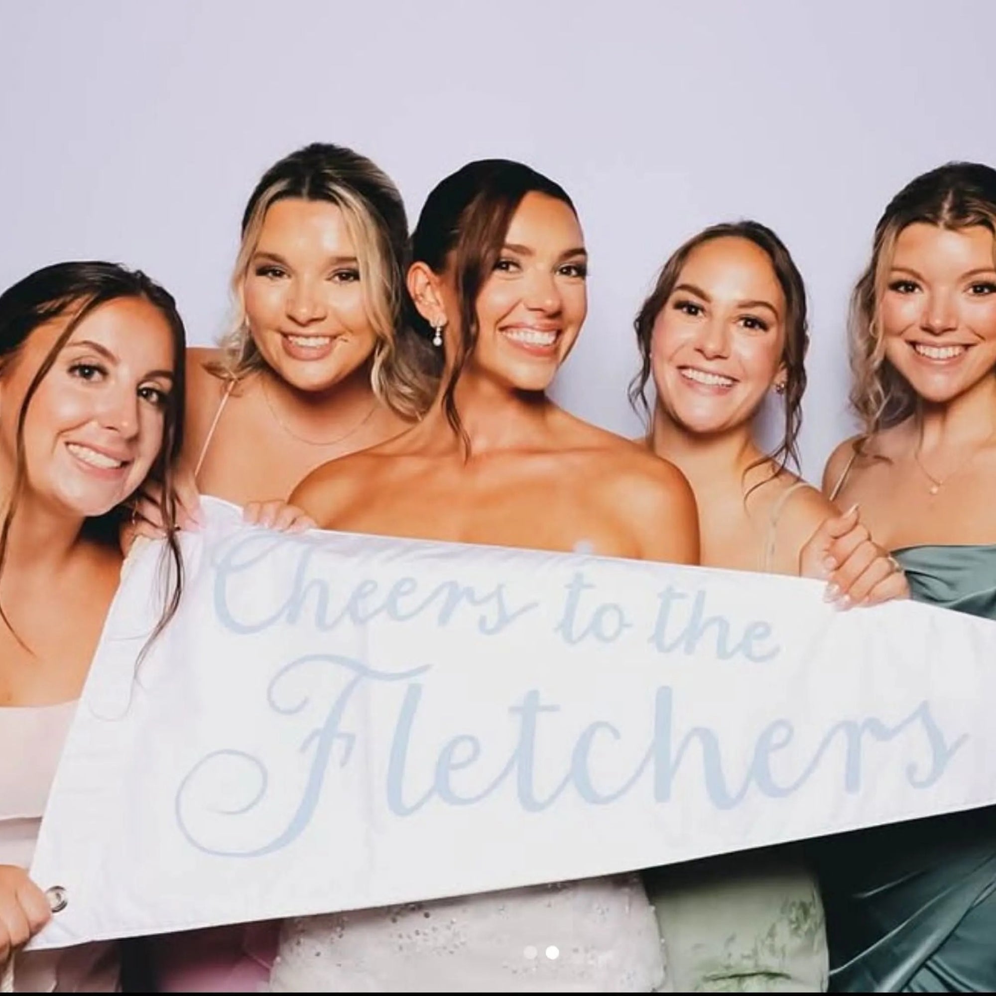 Five women holding a wedding pennant that reads 'Cheers to the Fletchers' against a plain background