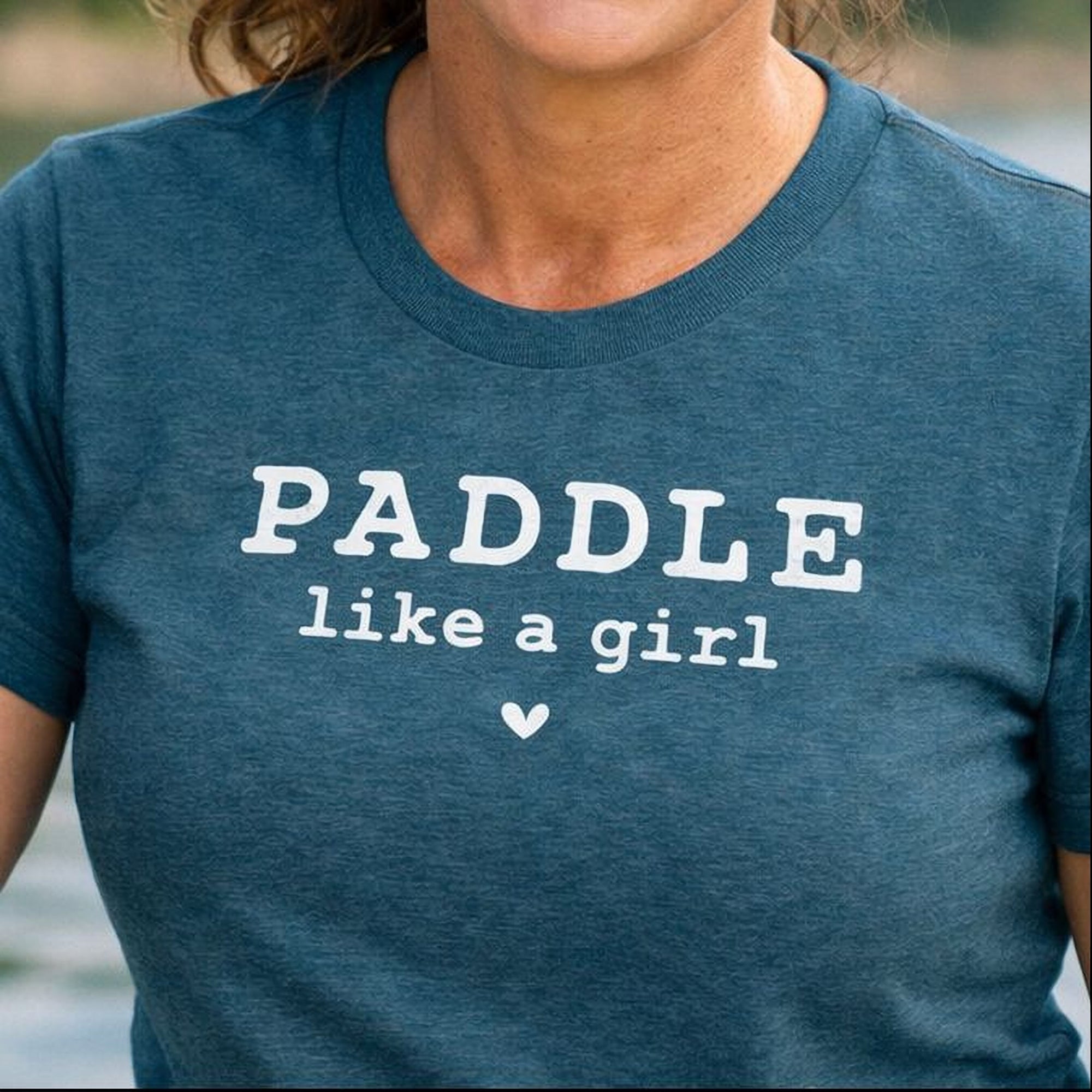 A woman wearing a blue Maine Salty Girl t-shirt with the text "PADDLING LIKE A GIRL" printed on it with a tiny heart.
