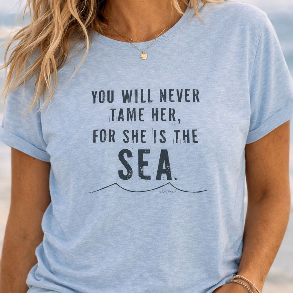 A woman wearing a light blue t-shirt with the text "You will never Tame her, for she is the sea" printed on it.