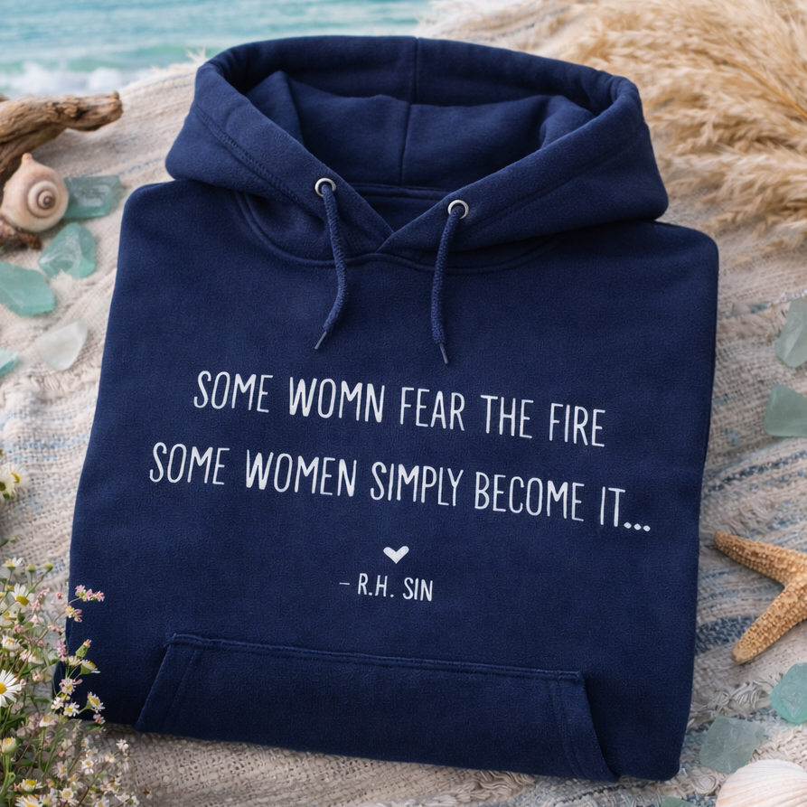 A navy blue hoodie with a quote printed on it, placed on a beach blanket with seashells and starfish nearby.