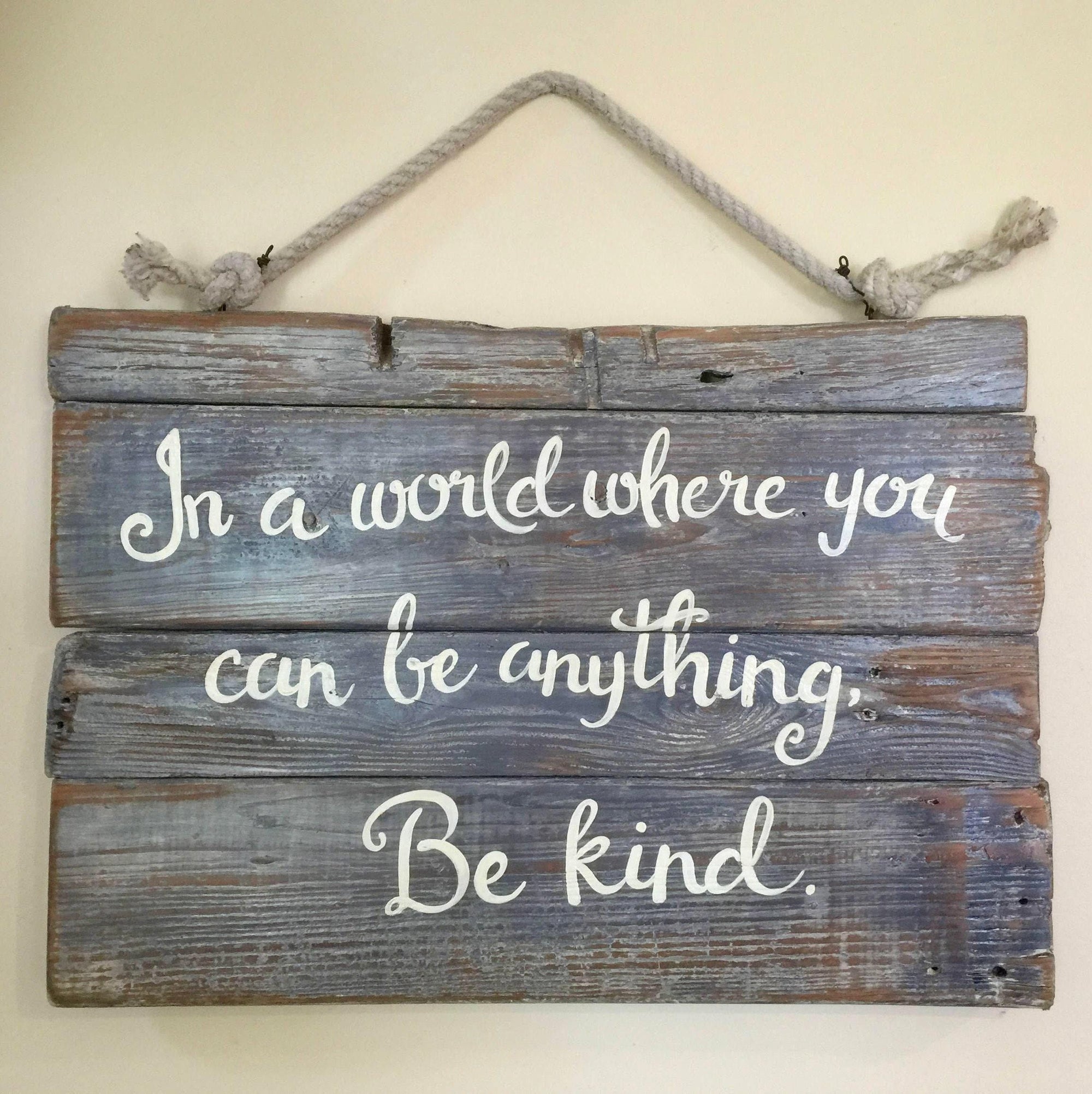 A wooden sign with the message "In a world where you can be anything, Be kind" written on it.