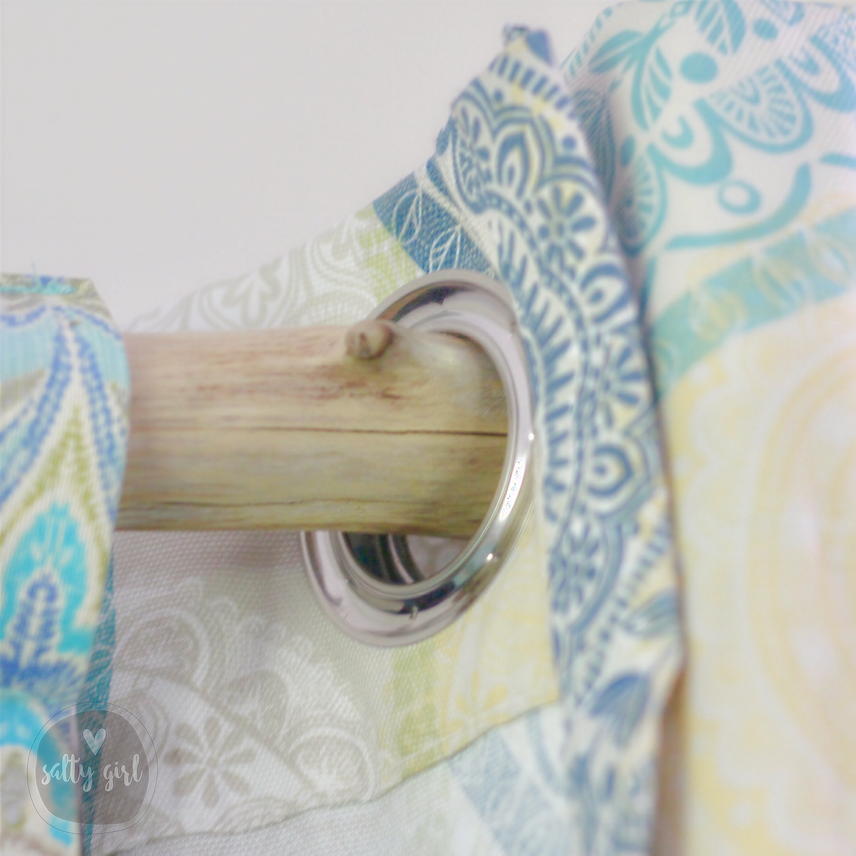 A wooden curtain rod with a decorative metal ring attached to it, set against a patterned fabric background.