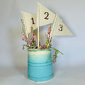 A blue vase with three white triangular flags, each displaying a number (1, 2, 3), is filled with pink flowers and greenery.