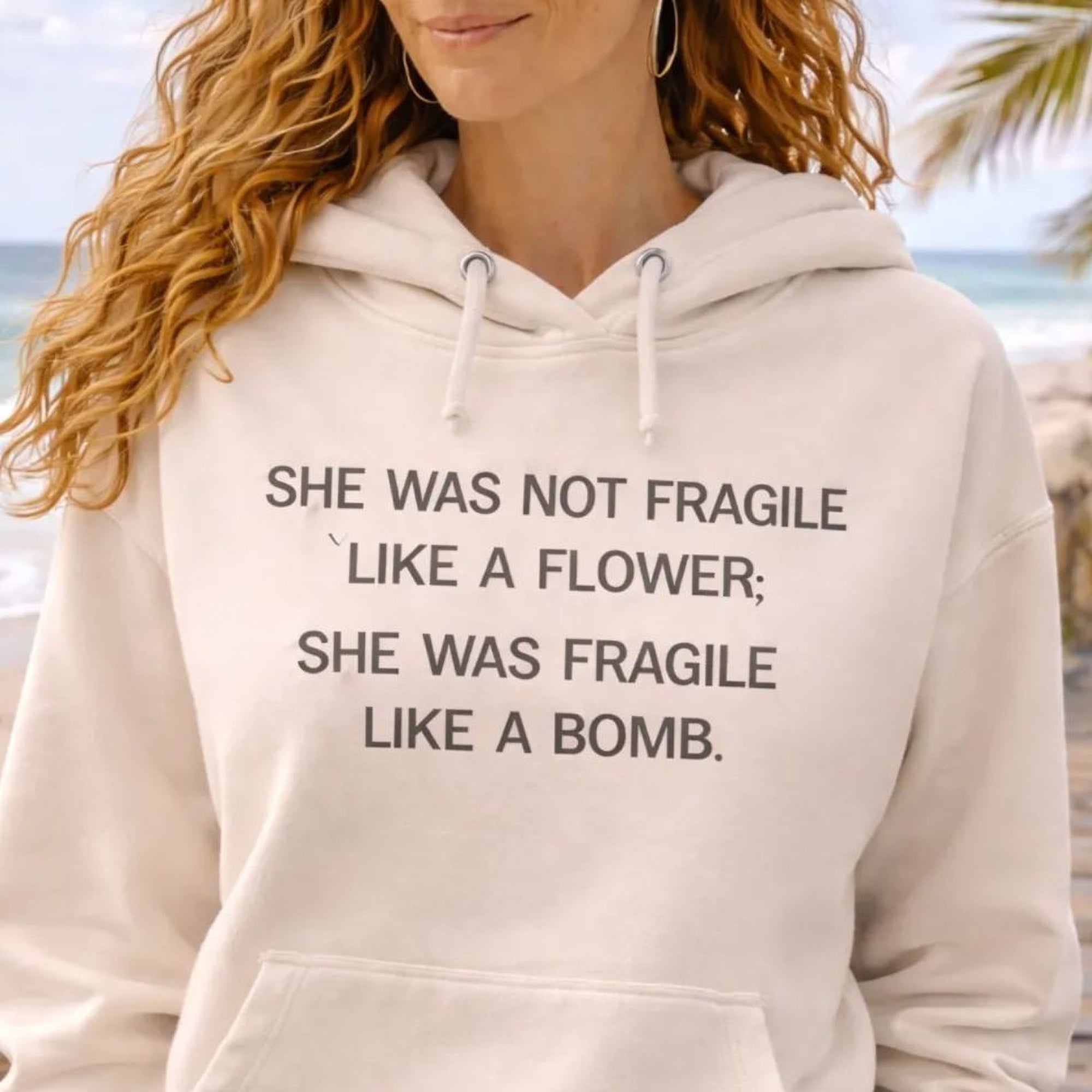 A woman wearing a white Maine Salty Girl hoodie with text printed on it, standing on a beach with palm trees in the background.