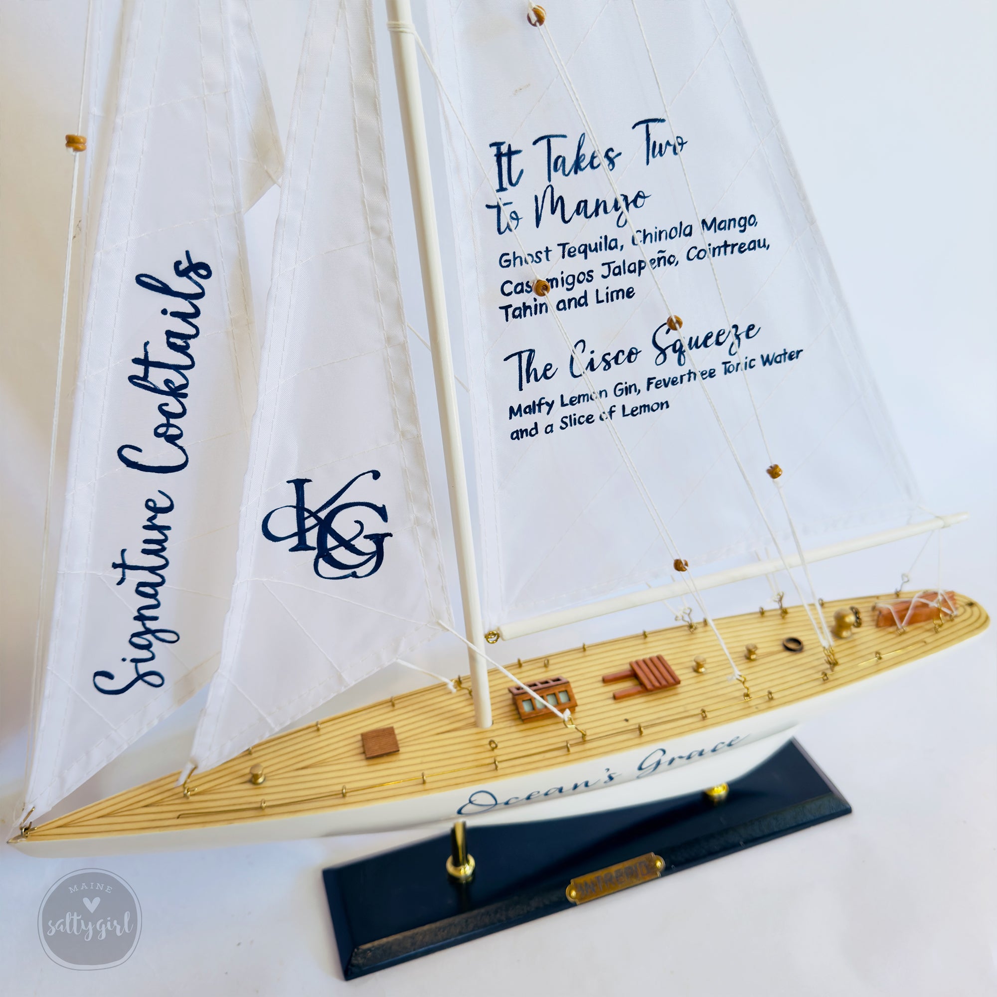 A model of a sailboat with a menu board on the deck, displaying various cocktail options.