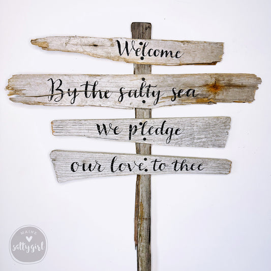 a wooden sign with a welcoming message, mounted on a wooden post.