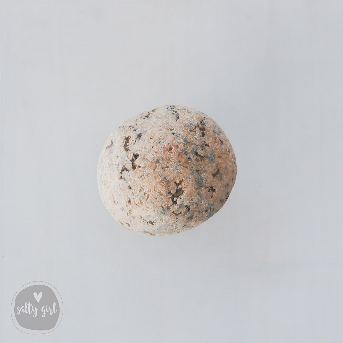A single, round, speckled rock is centered against a plain white background.
