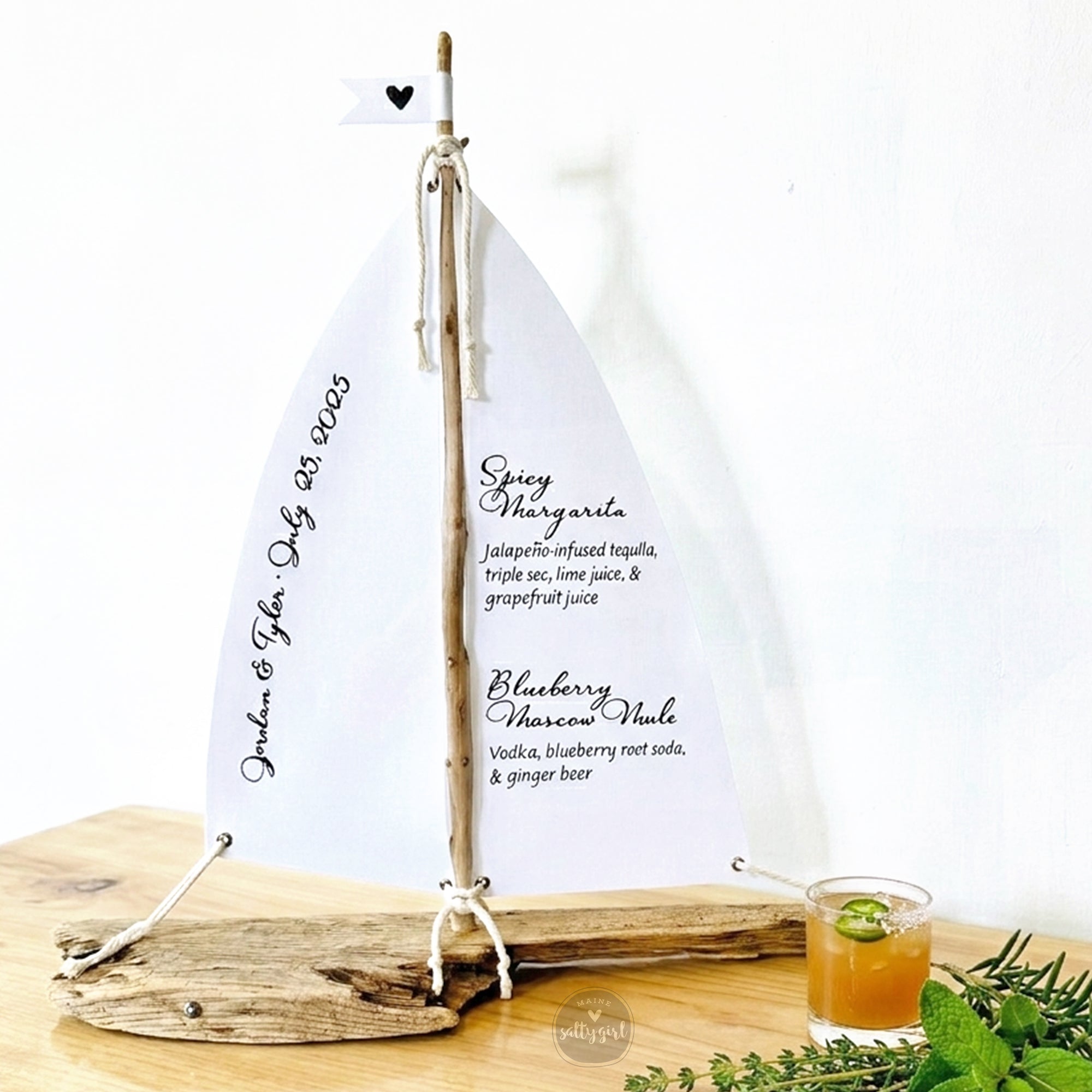 a white sailboat-shaped cocktail menu with a margarita and a sprig of mint on a wooden table.
