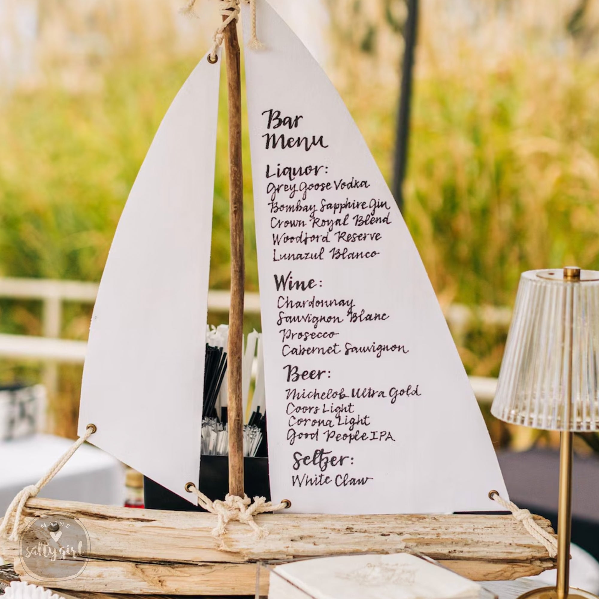 A wooden boat-shaped bar menu with a list of alcoholic beverages and a wine list, placed on a table with a lamp.
