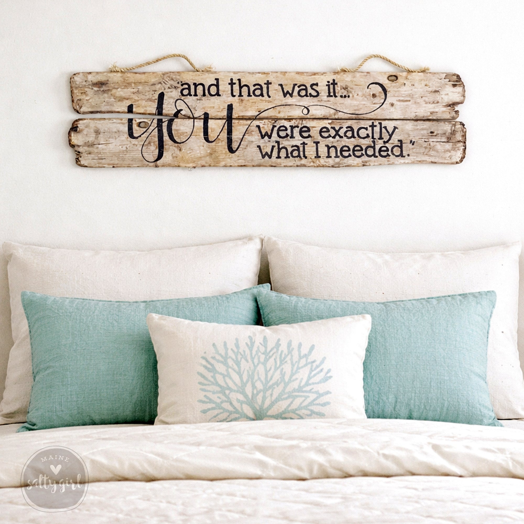a bedroom with a bed adorned with white pillows and a white comforter. Above the bed, there is a wooden sign with a message that reads "and that was it. You were exactly what I needed."