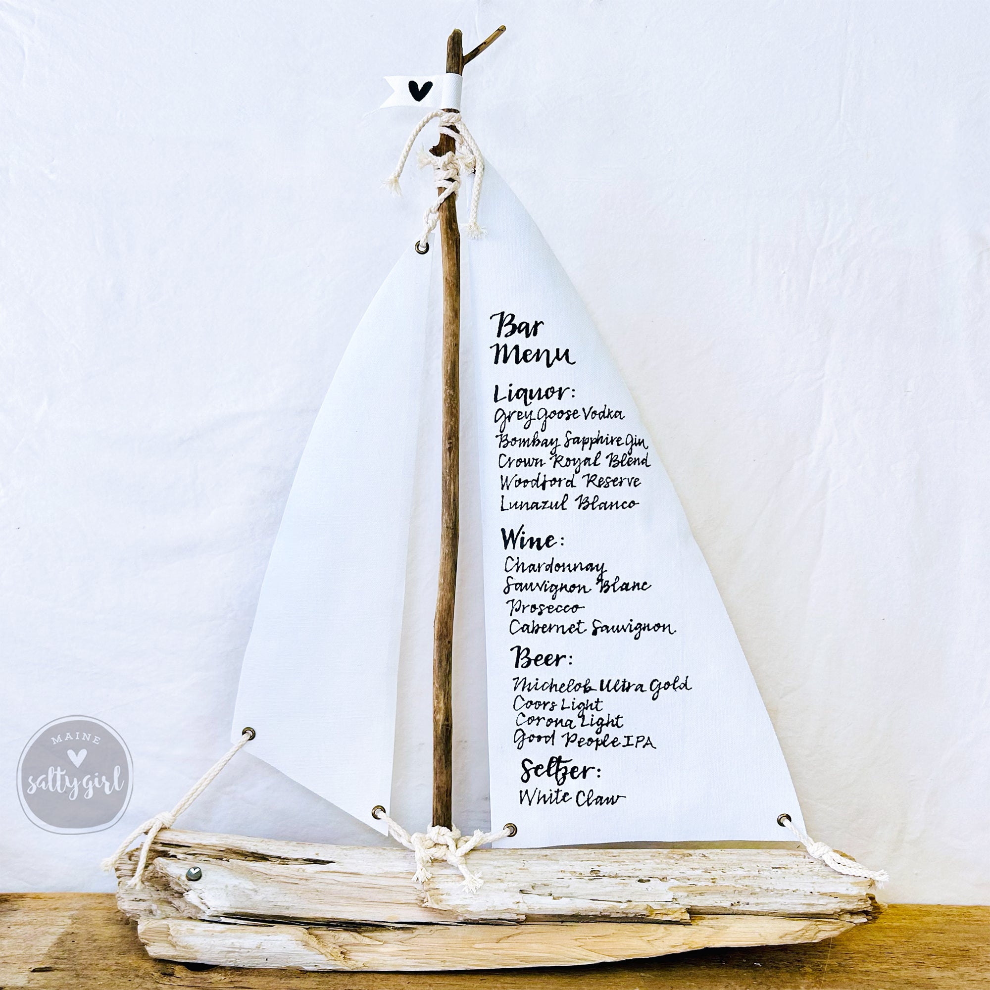 A white sailboat-shaped sign displaying a bar menu with various alcoholic and non-alcoholic drink options.