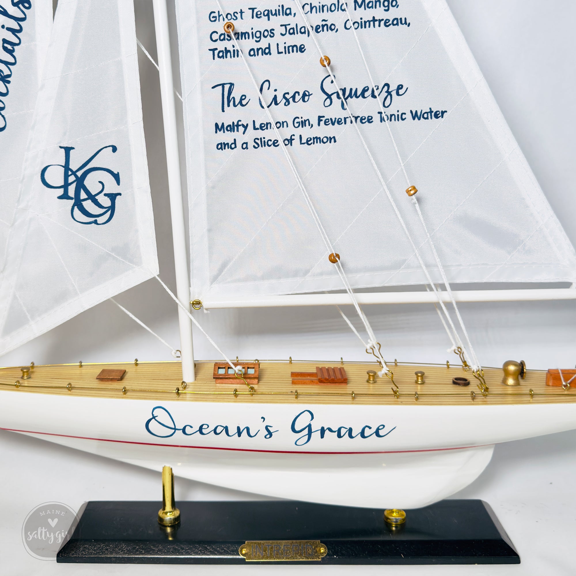 A model ship named "Ocean's Grace" with a white sail and gold accents, displayed on a black base.