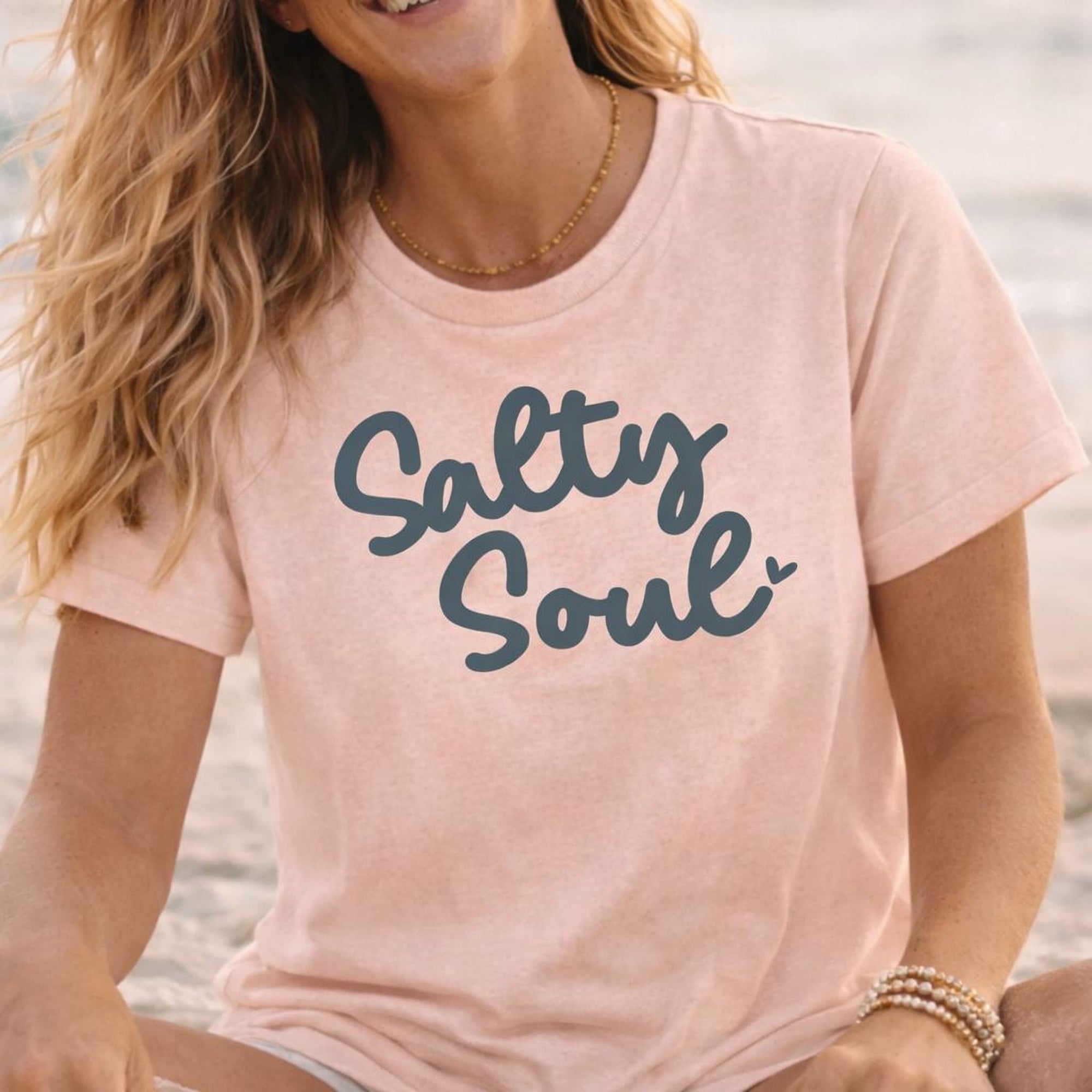 A woman wearing a pink t-shirt with the text "Salty Soul" printed on it, smiling at the camera.