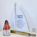 a white sailboat-shaped cocktail menu with a red and white striped cone on a white surface.