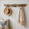 a rustic wooden coat rack with three hooks, displaying a hat, a scarf, and a pillow.
