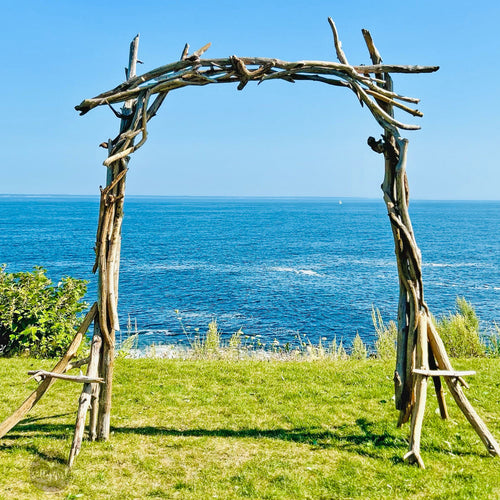 A rustic wooden arch stands on a grassy field, overlooking the vast ocean and clear blue sky.
