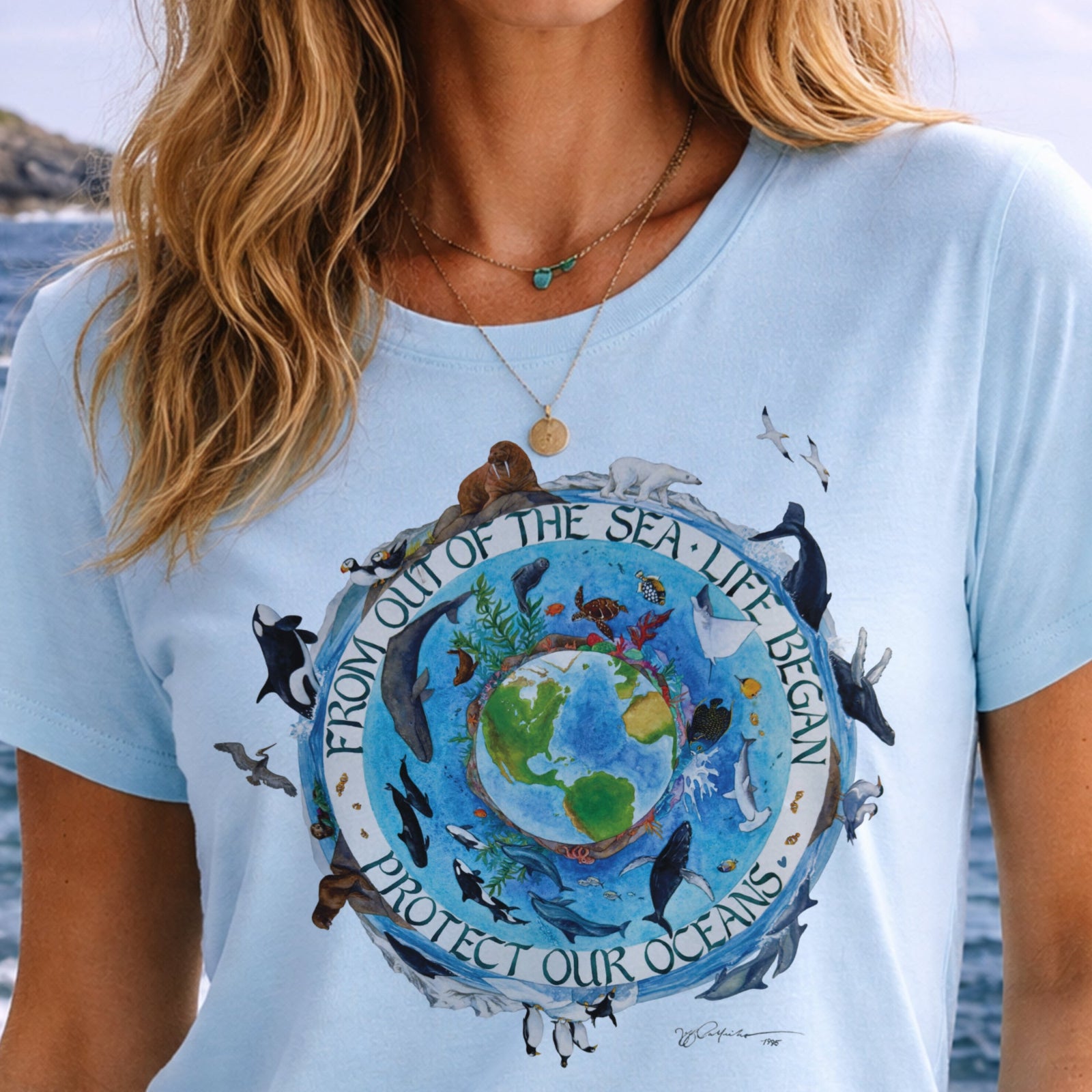 Light blue t-shirt with ocean-themed design and text, worn by a person with a blurred natural background.
