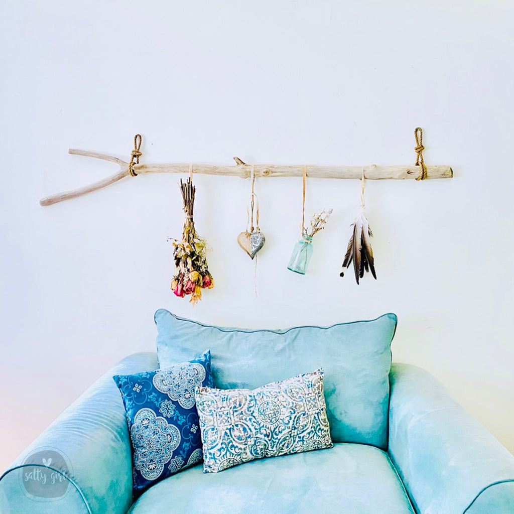A cozy living space with a blue couch adorned with patterned pillows, and a wooden branch hanging above it, displaying various decorative items such as a heart, feathers, and a vase.