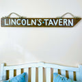 A wooden sign with the name "Lincoln's Tavern" hanging on a wall above a white wooden headboard.