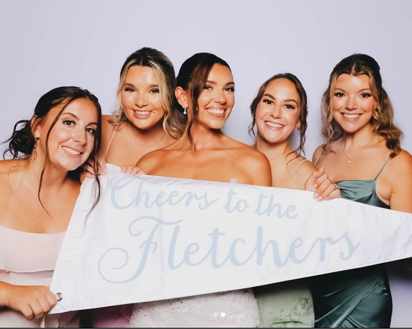 Five women holding a wedding pennant that reads 'Cheers to the Fletchers' against a plain background