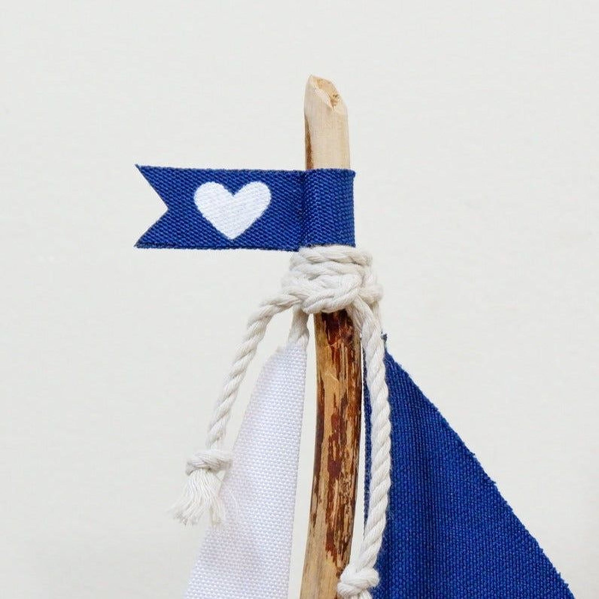 A blue flag with a white heart symbol attached to a wooden stick, tied with a white rope.