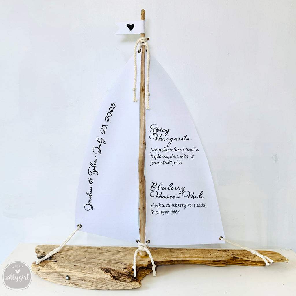 A white sailboat-shaped object made of driftwood, displaying a menu of alcoholic beverages.