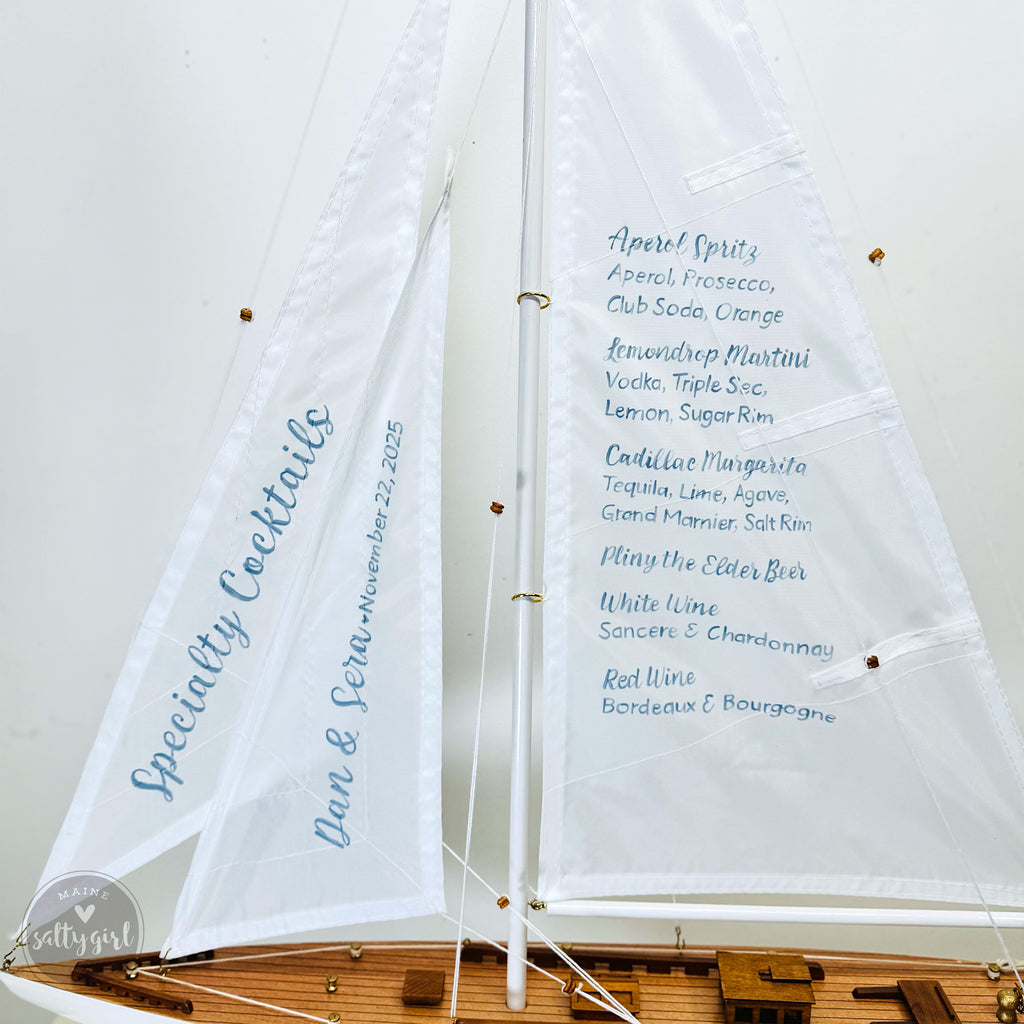 A white sailboat with a list of cocktail names on it, including Aperol Spritz, Club Soda, Orange, Lemon Drop, Triple Sec, Cointreau, Garnacha, and White Wine.