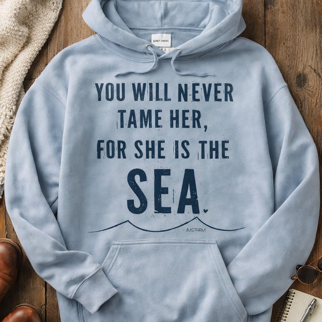 A light blue hoodie with the text "YOU WILL NEVER TAME HER, FOR SHE IS THE SEA" printed on it, along with a graphic of a wave.