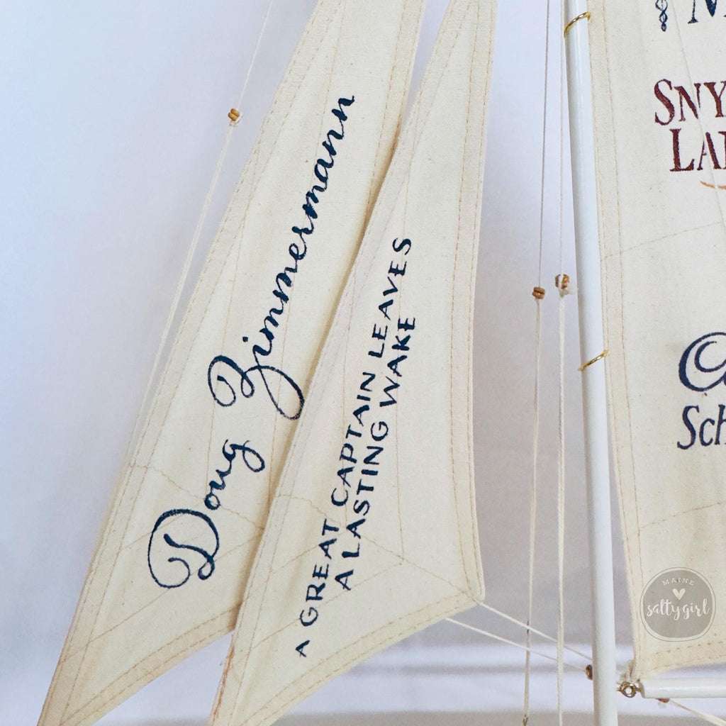 a close-up view of a sailboat with two sails, each displaying a name and a message.