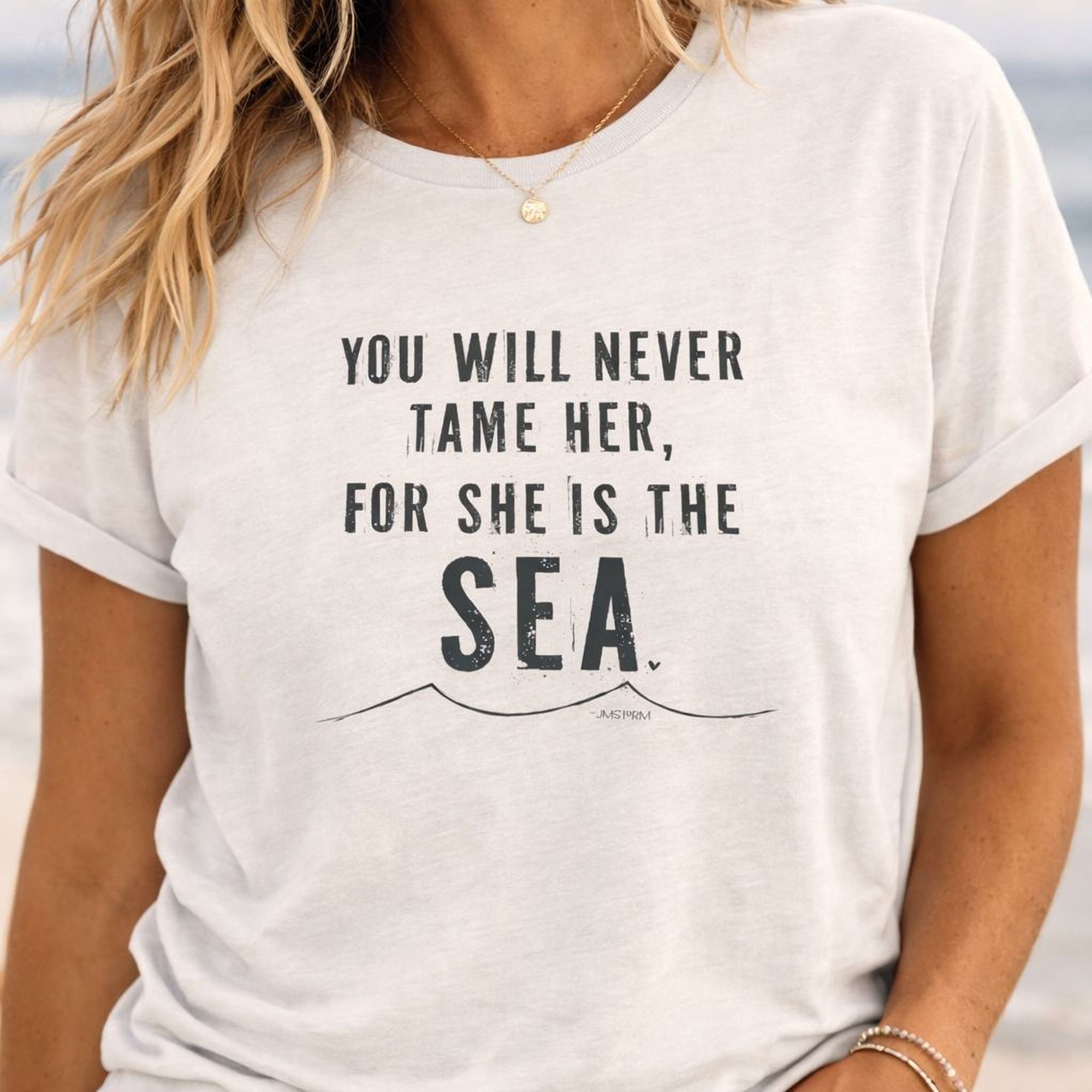 A white t-shirt with the text "YOU WILL NEVER TAME HER, FOR SHE IS THE SEA" printed on it.