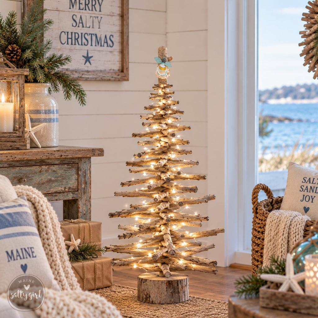 A rustic-style Christmas tree made from wooden branches, adorned with twinkling lights, stands in a cozy living room with a view of the ocean through a window.