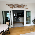 a modern living room with a large glass sliding door leading to another room. The sliding door is adorned with a wooden branch sculpture, adding a rustic touch to the space. The room features a white sofa, a coffee table, and a dining table with chairs. The overall design and decor create a harmonious and inviting atmosphere.