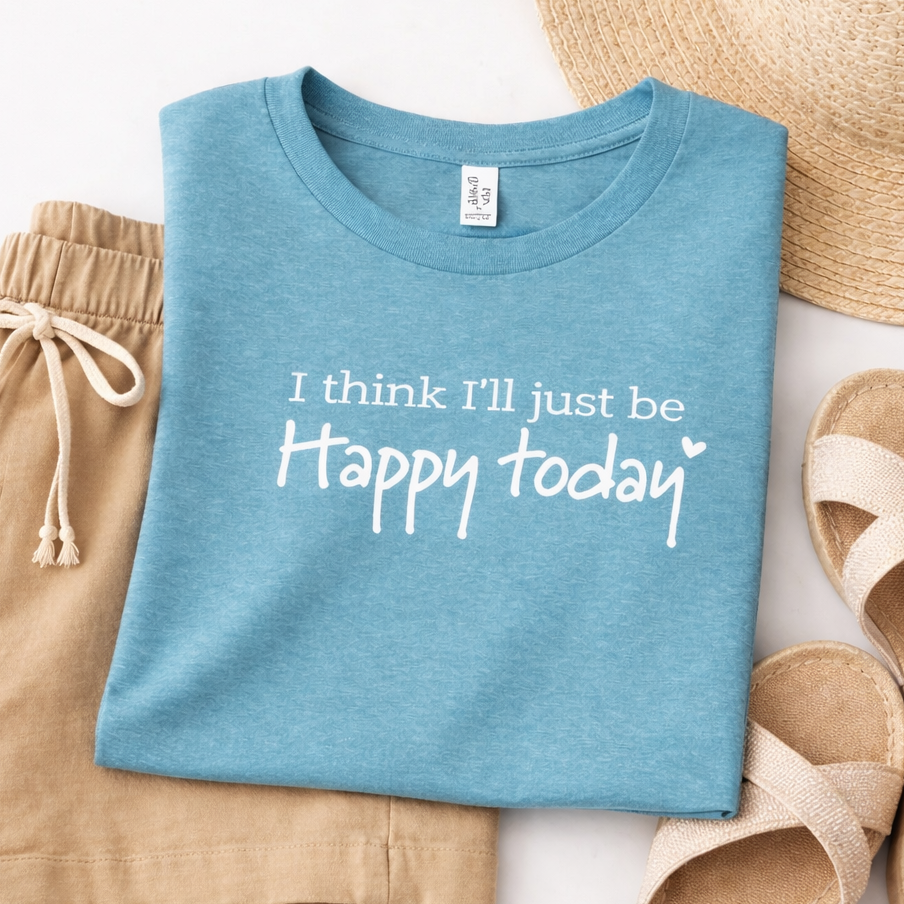 A blue t-shirt with the text "I think I'll just be happy today" printed on it, along with a straw hat and sandals, all laid out on a white background.