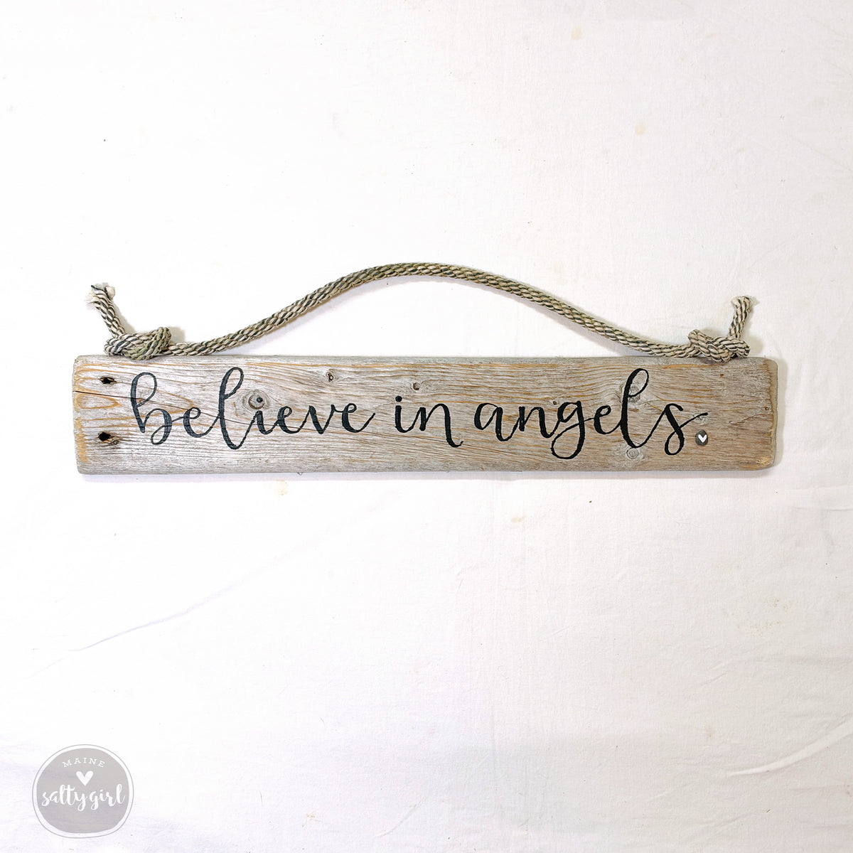 A wooden sign with the text "Believe in angels" written on it, hanging from a rope.