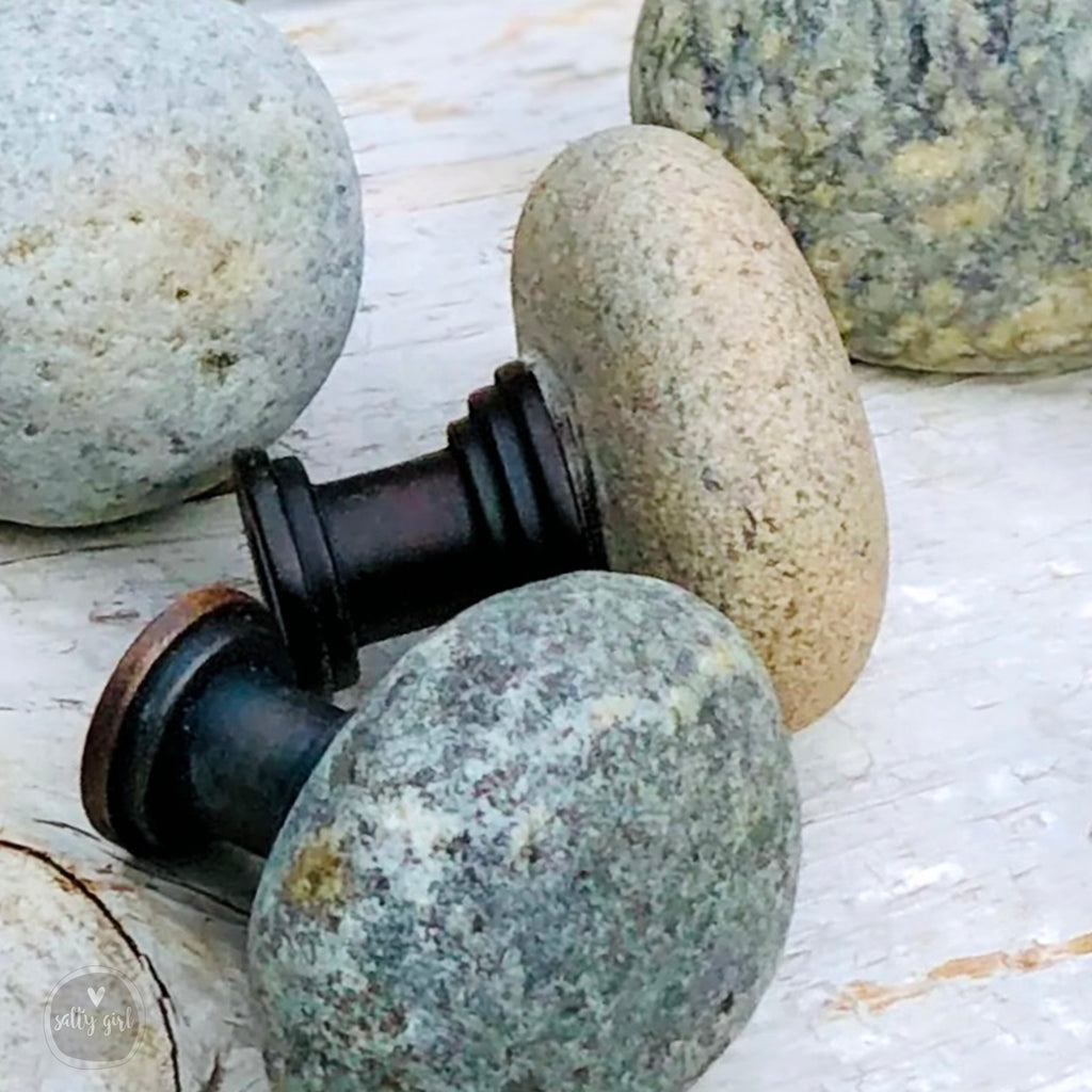 a collection of variously shaped and colored rocks and stones, including a black metal knob and a gray stone, arranged on a wooden surface.