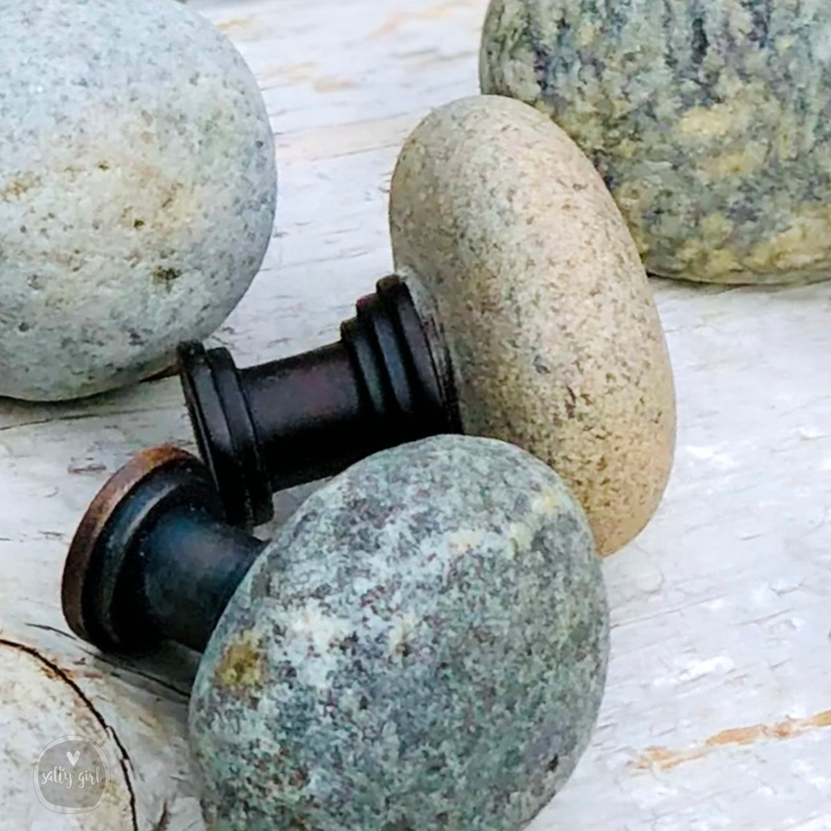 a collection of variously shaped and colored rocks and stones, including a black metal knob and a gray stone, arranged on a wooden surface.