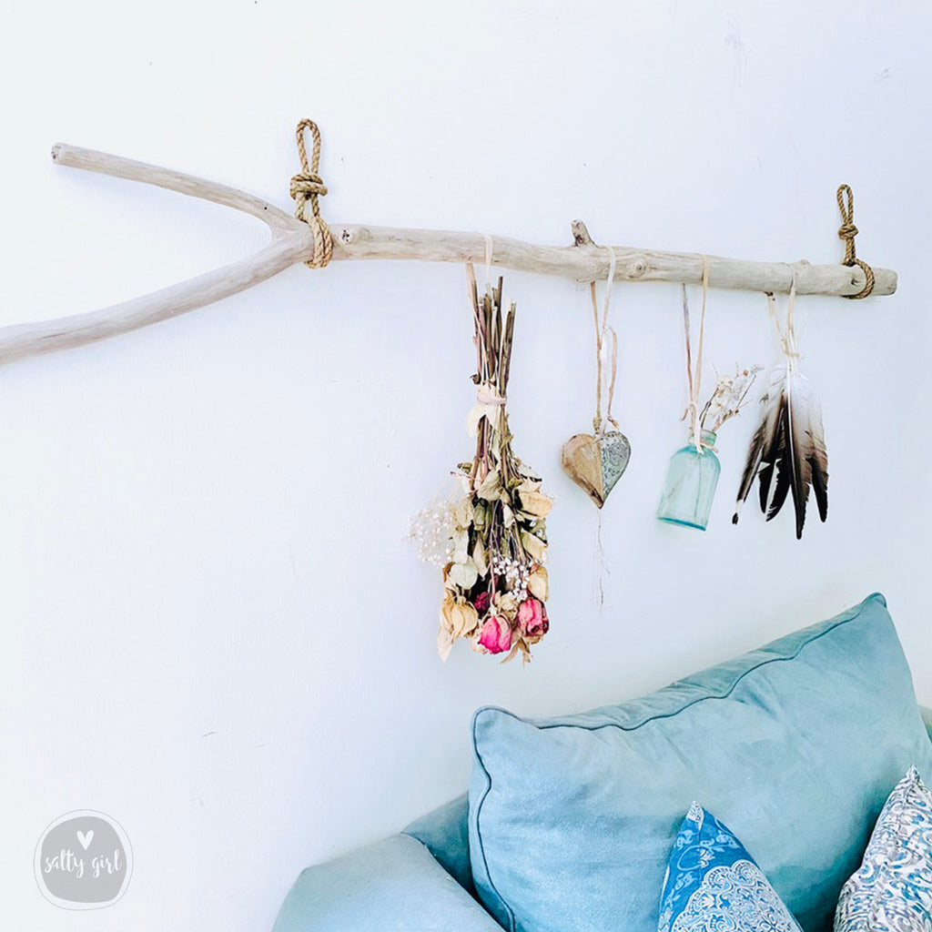 a cozy living space with a blue couch and a rustic branch with dried flowers and feathers hanging on it.
