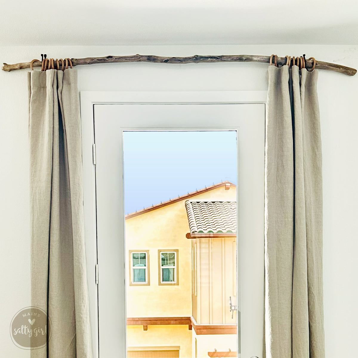 a view from a window, with a wooden branch hanging from the ceiling and a yellow building visible through the window.