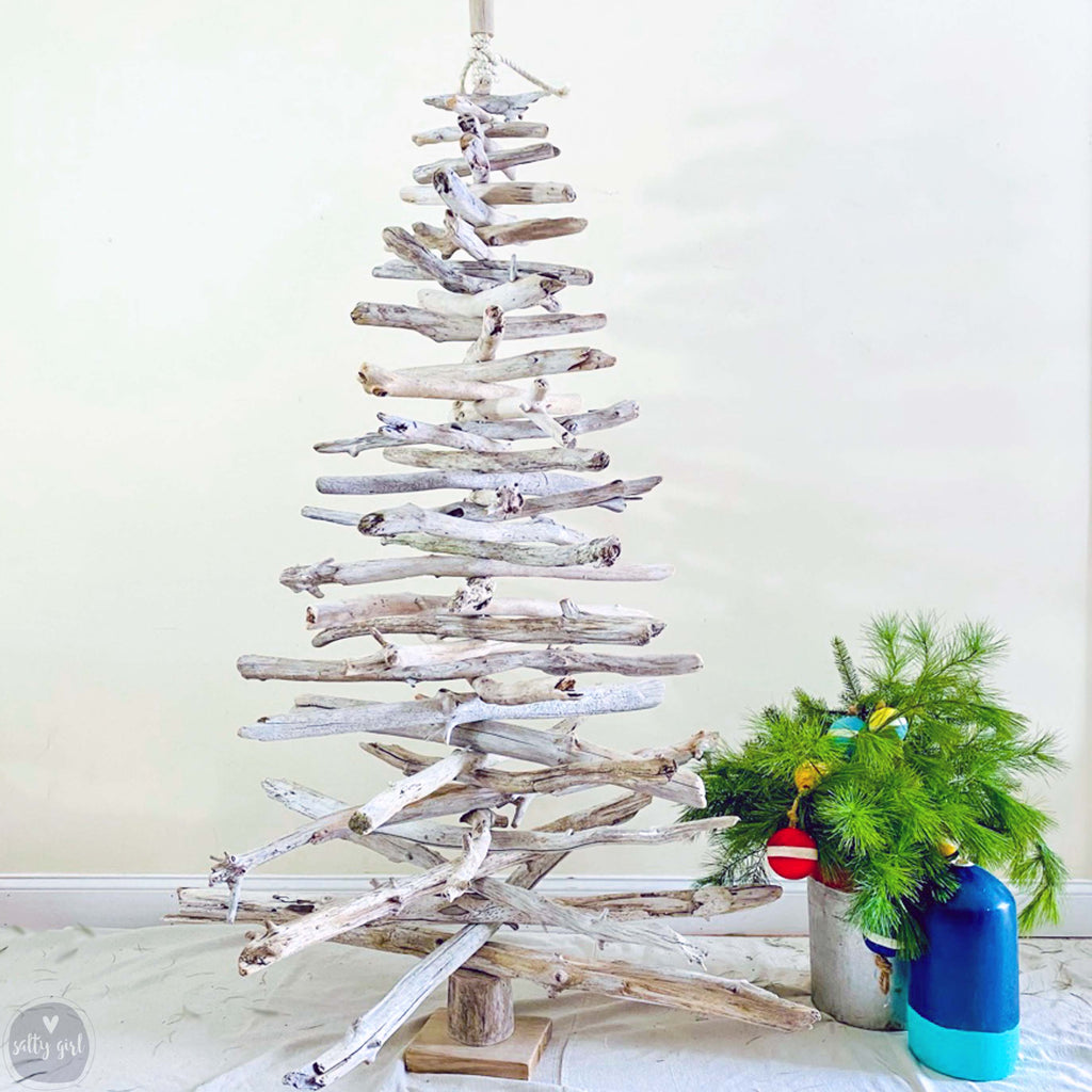 A unique, handcrafted driftwood Christmas tree stands in the center of the image, surrounded by a potted plant and a blue vase, creating a festive holiday scene.