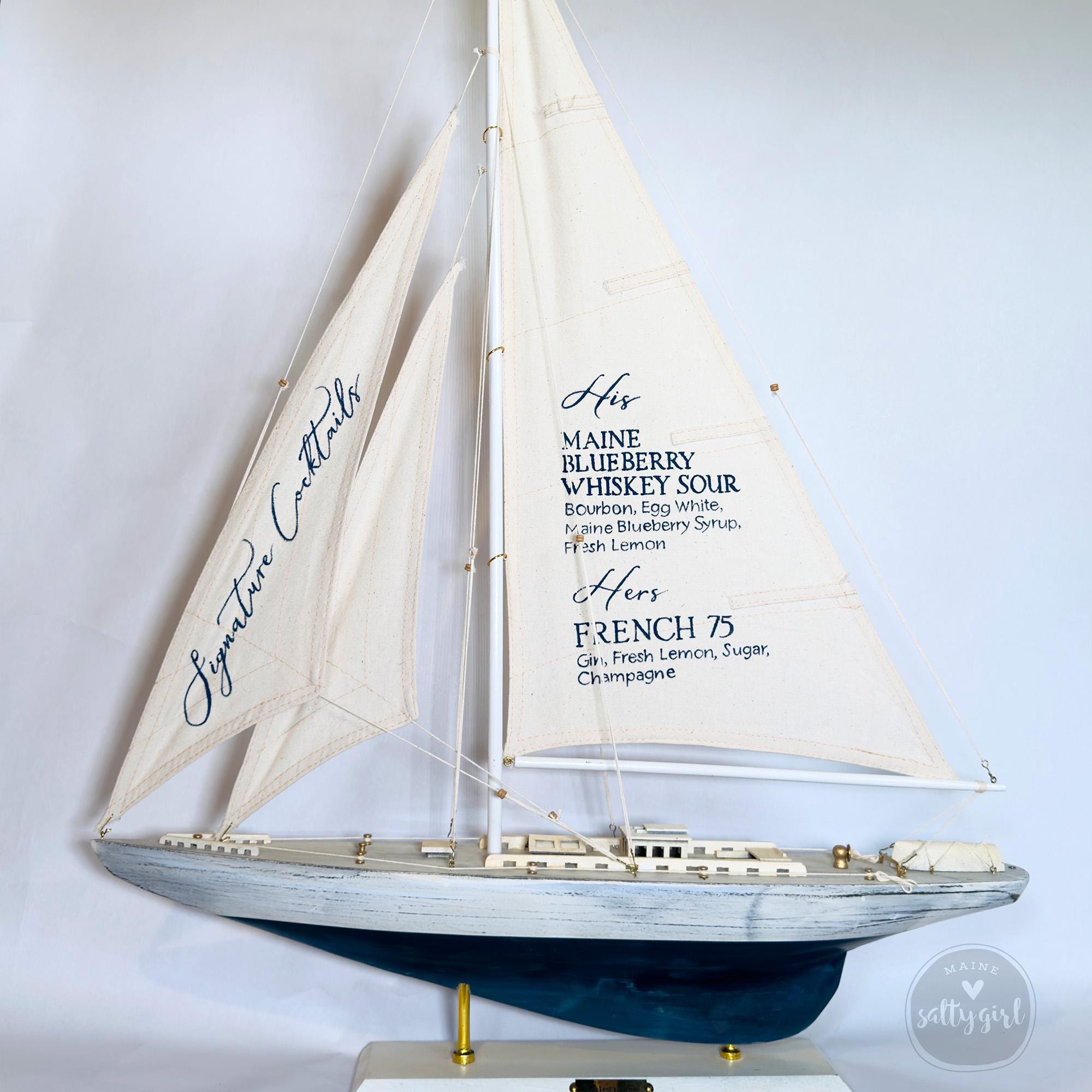 A model of a sailboat with a white sail and blue trim, featuring text that lists the names of the different wines and champagne that are served on the boat.