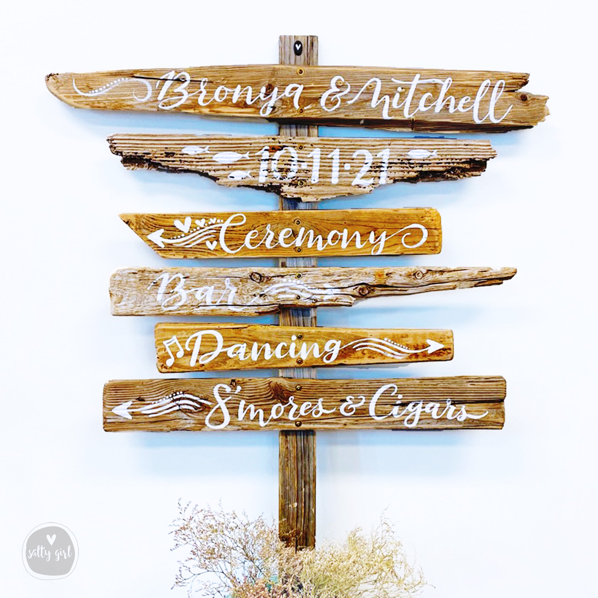 A wooden sign with various event details written on it, including the names 'Bronya & Mitchell' and the dates '11-21'.