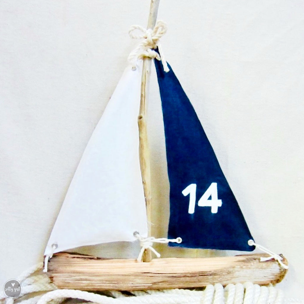 A small wooden sailboat with a white sail and a blue sail, displaying the number 14.