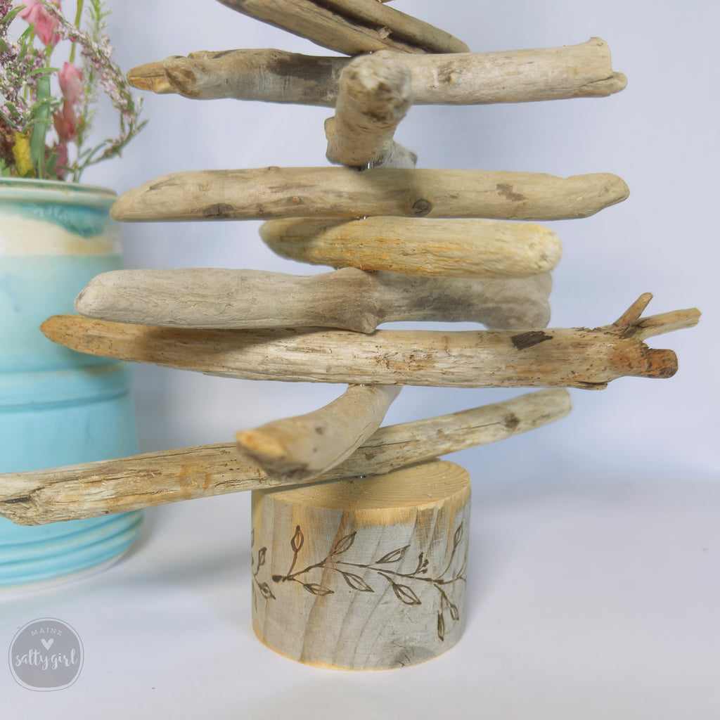 A rustic driftwood tree made of various branches and logs, displayed on a wooden base with a leaf design.