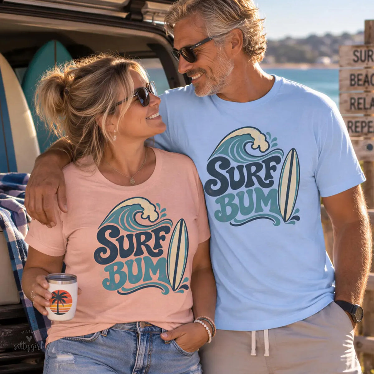 A man and a woman are standing together, smiling and posing for a photo. They are both wearing matching t-shirts with the text "Surf Bum" printed on them.