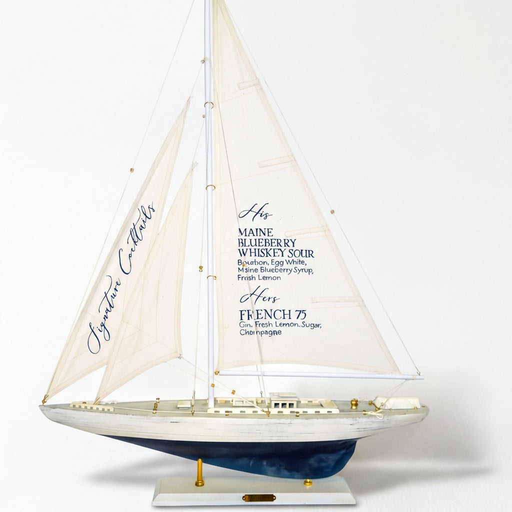 A model of a sailboat with a white sail and blue hull, featuring text on the sail that lists various alcoholic beverages.
