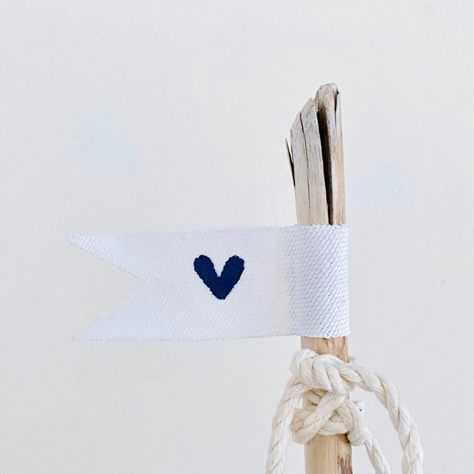 A white flag with a blue heart symbol is attached to a wooden stick, which is tied with a rope.