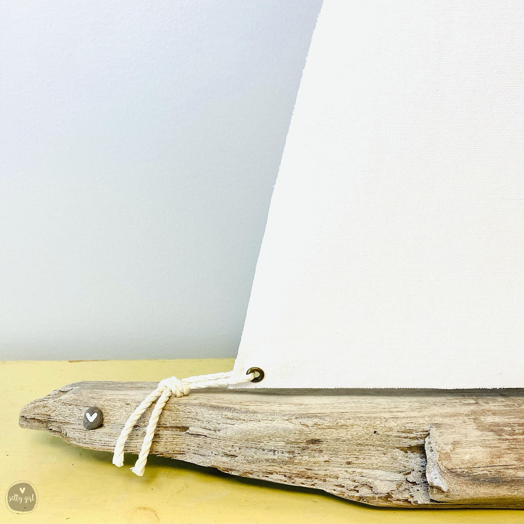 A wooden sailboat made from driftwood, with a white sail and a small heart-shaped ornament attached to the front.